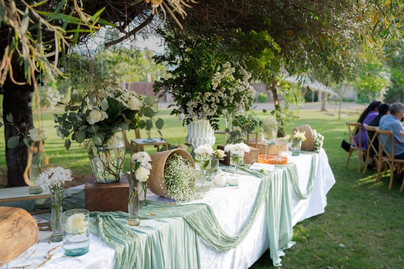 Mesa decorada con flores blancas y mantel verde salvia en el jardín