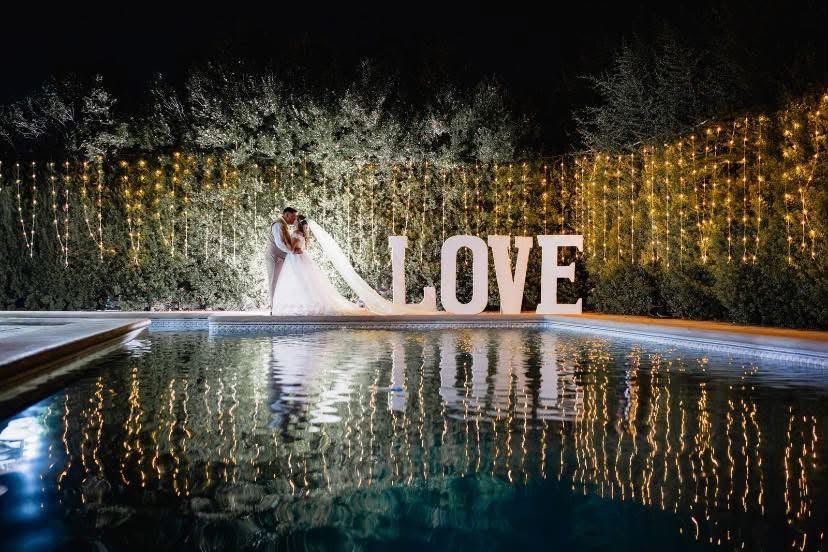 Novios junto a la piscina con letras LOVE y cortina de luces
